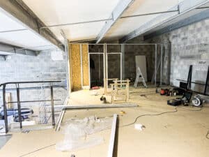 Chantier intérieur : murs en blocs gris "EnBloc", ossature métallique pour cloisons OSB, outils au sol (laser vert, échelle) et plafond à panneaux. Travaux en cours.