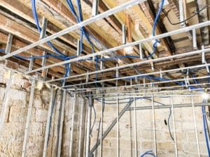 Chantier de rénovation: ossature métallique, solives apparentes, plomberie PEX bleue et câbles électriques.