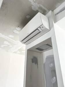 Climatiseur Daikin blanc fixé au mur d'une pièce en rénovation. Le plafond brut et les murs enduits indiquent un chantier.