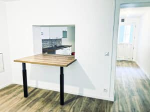 Cuisine moderne ouverte avec passe-plat et comptoir rabattable en bois clair, sol en parquet. Design épuré et fonctionnel.