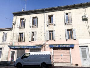 Façade de bâtiment européen avec volets vieillis, enseignes "TELE EXPRESS" et van blanc garé. Détails des câbles et AC unit.