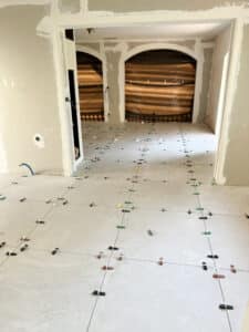 Intérieur en rénovation : carrelage clair posé au sol avec système de nivellement. Murs et arches en cours de finition, chantier actif.