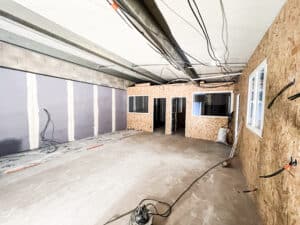 Pièce en cours de rénovation pour bureaux. Murs en placo et cloisons en OSB avec portes et fenêtres. Plafond exposé avec câbles, sol béton, pompe.