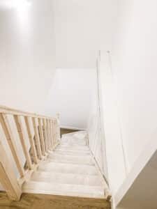 Escalier intérieur blanc en bois avec rampe claire, recouvert de protection, dans une maison en rénovation lumineuse.
