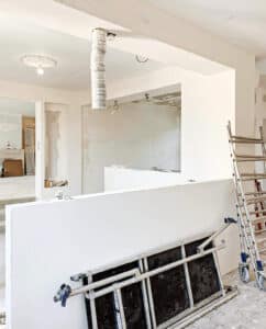 Intérieur d'une maison en rénovation avancée avec murs blancs, un lustre suspendu et un échafaudage métallique sur une cloison.