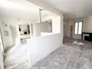 Intérieur en rénovation : murs blancs, sol en bois marqué de peinture, panneau électrique. Demi-cloison, conduit au plafond et deux cheminées.