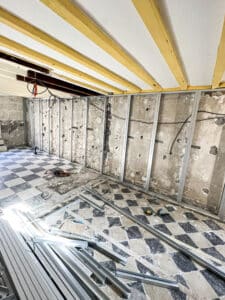 Chantier de rénovation: plafond à poutres jaunes et blanches, murs avec ossature métallique pour placo (MONTANT), câbles et carrelage damier au sol.
